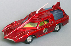 The photograph depicts a scale toy replica of an unarmoured, futuristic car that is deep red in colour and incorporates an angular bonnet and roof.