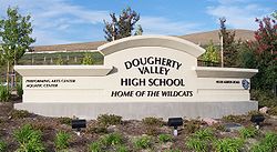 A beige school sign, reading "Dougherty Valley High School", and then underneath in smaller italicized text, "Home of the Wildcats". To the left are even smaller texts reading "Performing Arts Center" and "Aquatics Center", and to the right are the school's address and a wildcat logo.