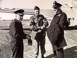 Three-quarter informal portrait of three men in military uniforms in front of the left wing of a twin-engined military monoplane