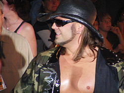 Adult white male wearing a black cowboy hat and a camouflage jacket.