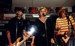 Magnapop performing in a record store with flyers for their album tacked on the wall behind them