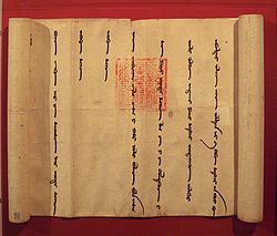 A partially unrolled scroll, opened from left to right to show a portion of the scroll with widely spaced vertical lines in the Mongol language. Imprinted over two of the lines is an official-looking square red stamp with an intricate design.