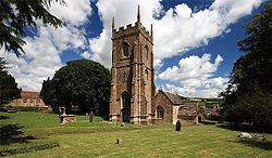 Stone building with square tower. In the foreground is a garssy area with gravestones.