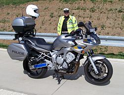 Gray police motorcycle, with policeman standing behind it