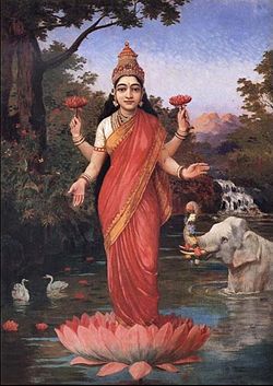 A woman wearing red and gold clothes,standing in a lotus that is on water, has four arms, and is holding a lotus in her back hands.