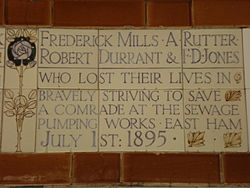 A tablet formed of five tiles of varying sizes, bordered by yellow and blue flowers in an art nouveau style. The tablet reads "Frederick Mills, A Rutter, Robert Durant & F. D. Jones who lost their lives in bravely striving to save a comrade at the sewage pumping works, East Ham July 1st 1895".