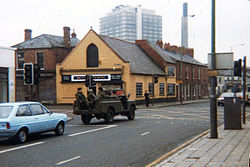 A picture of a city street with an army vehicle in the road.