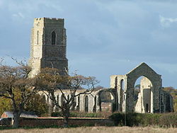 The ruins of a stone church seen from the southeast showing the walls of the chancel and south aisle, with the intact tower beyond