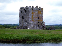 A castle in the centre, grass and water in the foreground, sky and landscape in background