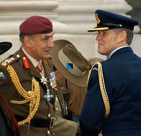 Two men in military uniforms—one blue and one green—standing in front of a stone monument