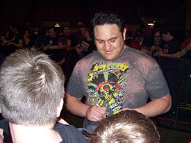 A dark-skinned adult male wearing a muti-colored T-shirt signing an autograph