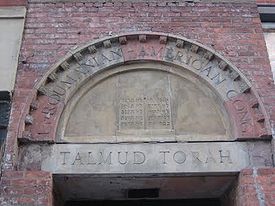 Stones over a doorway arch with the incomplete name "Roumanian-American Cong" in carved capital letters. Beneath, carved into the lintel, are the words "Talmud Torah", also in capital letters. The two surround a carving of two tablets with Hebrew writing, representing the Ten Commandments.