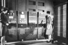 Two women operating the ENIAC's main control panel. Switches and panels occupy an entire wall.
