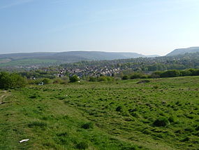 Across the overgrown site of the fort wher no walls remain with the hills of Tintwistle and Peak Naze behind