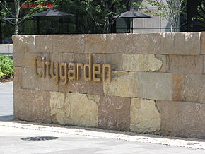 The word "Citygarden" in gold metal letters is fixed to a low wall made of golden-yellow rock bricks.}}
