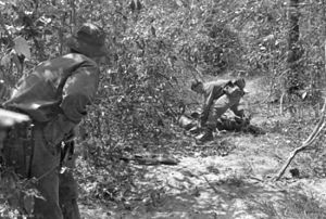 Black and white image of an Australian soldier searching the body of a dead Viet Cong while another soldier provides cover