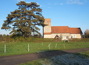 A stone church seen from the south with red tiled roofs and a plain tower on the left