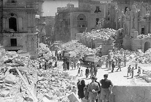 Service personnel and civilians clear up debris on a heavily bomb-damaged street in Valletta, Malta on 1 May 1942