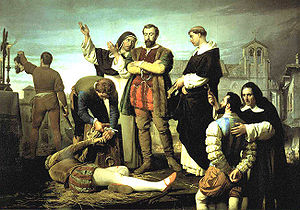 Two men and a priest stand in the center, overseeing the proceedings.  A dead body lies on the ground; a man triumphantly lifts up his severed head in the background.  A bearded man with hands bound is being brought forward to be executed next.