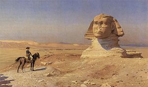 Small figure on a horse looks towards a giant statue in the desert, with a blue sky