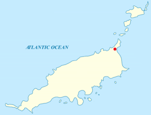 Map of an archipelago in the Atlantic Ocean. The main island is rod-shaped, oriented approximately west-southwest to east-northeast, with some irregular features in the coastline. A red label at the northeastern tip. Off the southern coast are nine smaller islands. Off the northeastern tip of the main island are five other smaller islands.