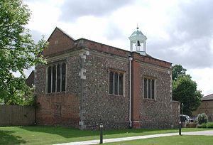 A flint and brick chapel seen from an angle, with a brick gable at the near end, and a white bellcote towards the far end