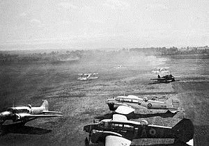 Three twin-engined military monoplanes parked on a landing field, with other aircraft in the background