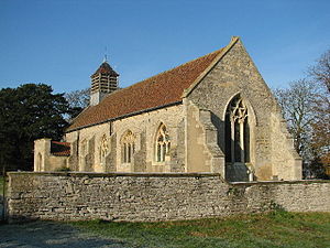 A stone church with a red tiled roof seen from the southeast.  It has a south porch and a louvred belfry at the west end; there is no external division between the nave and the chancel