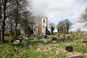 A stone church from the east seen at a distance in a churchyard, showing the east window and a battlemented west tower