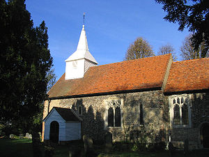 A flint church with red tiled roofs and a white wooden spire