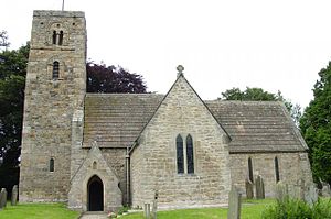A stone church seen from the south with a prominent south transept, a smaller porch to its left, and on the extreme left a tower