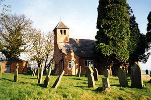 A chapel with a pyramidal roof seen beyond gravestones in a churchyard