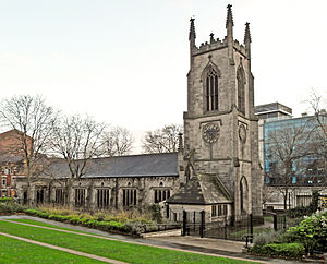 A substantial stone church seen from the northwest.  The tower has crocketted pinnacles, and the north wall of the body of the church has a series of large rectangular windows