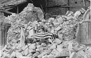 The flag-draped coffin of Maj. Thomas Howie rests on the rubble of the cathedral in St. Lo. (National Archives)