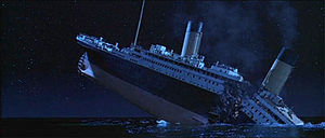The Titanic about to sink into the ocean, with the ship breaking into two parts and with smoke still coming out of the funnels.