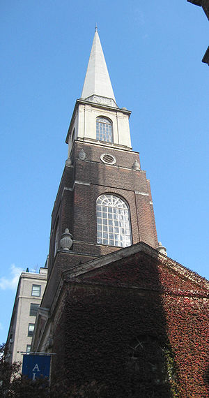 A brick church steeple with pointed wooden upper stage seen from below.