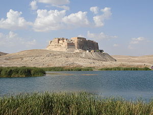 A massive stone structure on top of a hill on the edge of a lake