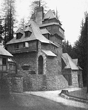 A monochrome photograph of a 75-foot-tall multi-room building with castle-like features, made of river rock, with many steeply pitched roof elements.