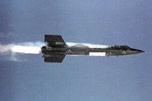 Black rocket aircraft with stubby wings and short vertical stabilizers above and below tail unit in-flight
