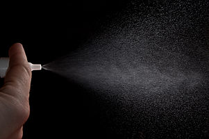 A hand sprays a mist of nasal spray from a pump.