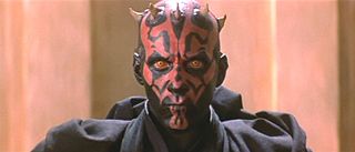 Heads and shoulders shot of a man wearing black robes. He is bald and has horns on his head, his face is covered in black and red tattoos, and his eyes are yellow.